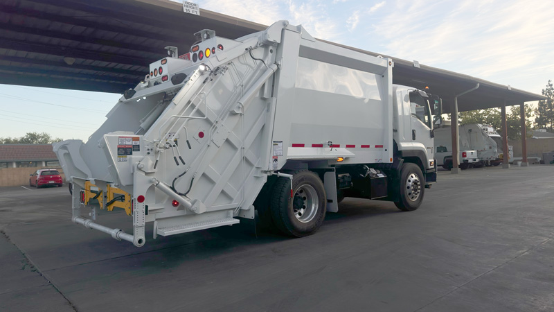 Rear loader refuse truck parked under canopy