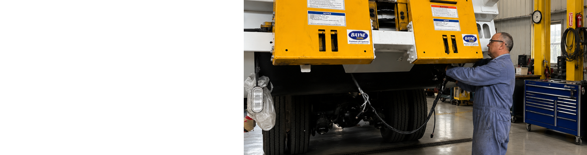 Technician servicing a yellow refuse truck in a maintenance shop